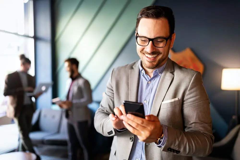 A man standing in his office, comfortably using his phone.