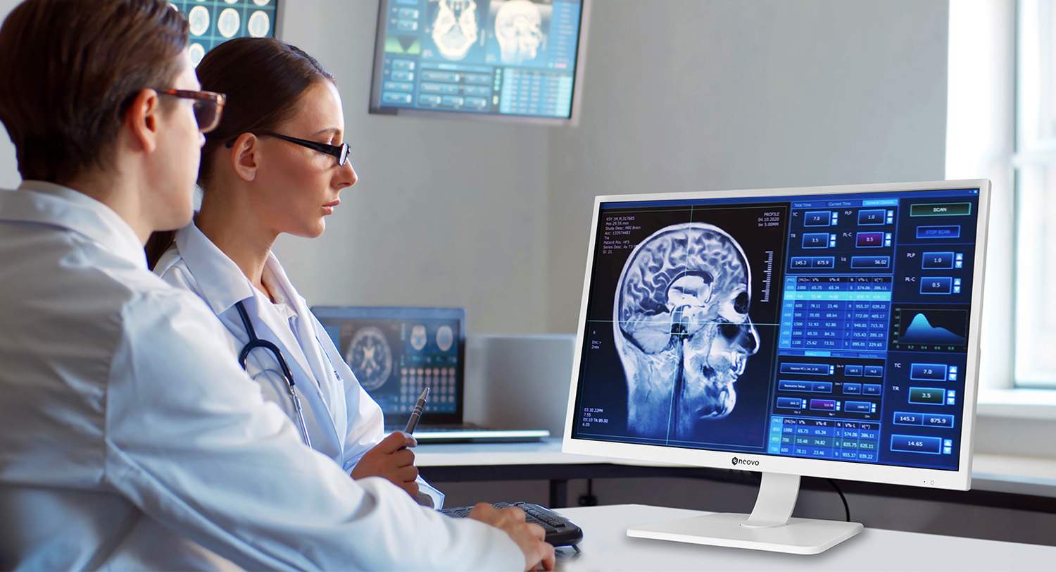 In a medical office, two doctors are analyzing a brain scan on a computer monitor, utilizing signal boosters for remote healthcare to ensure they have access to the most precise data and insights.